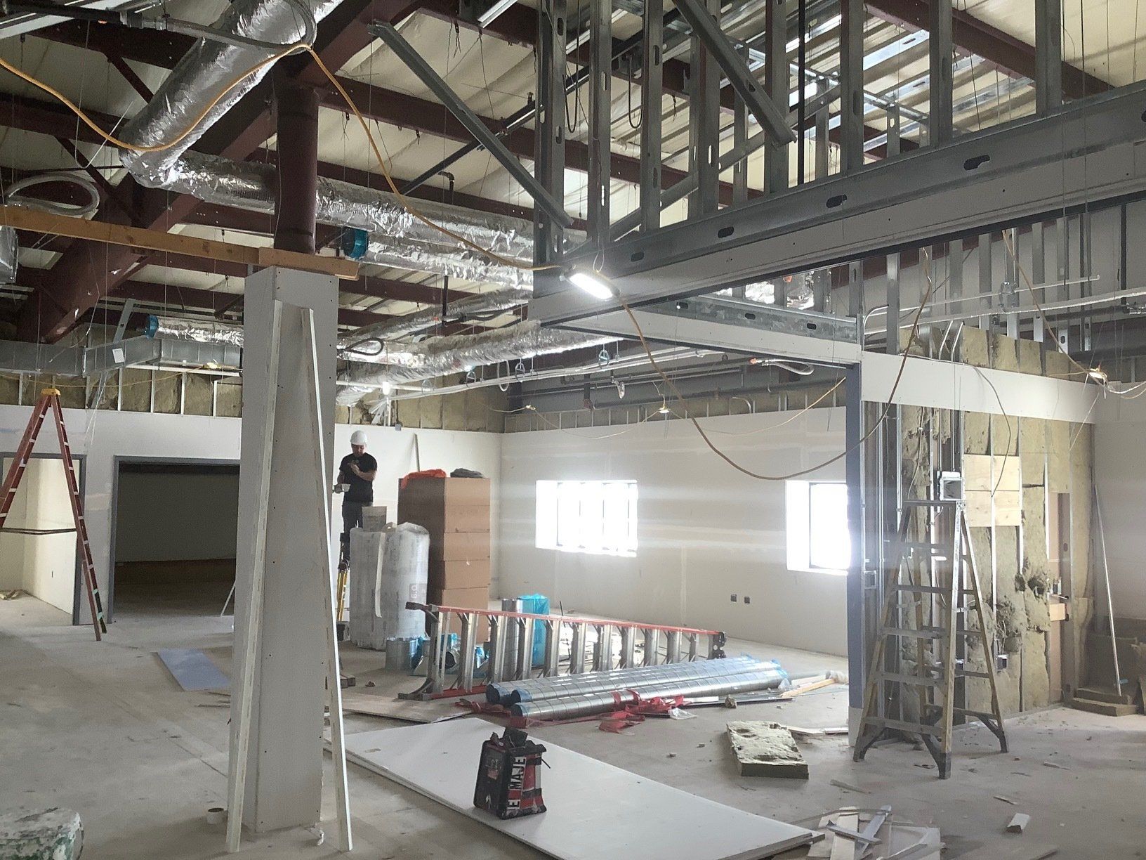 Interior construction site with exposed ceiling beams and walls, workers, and building materials.