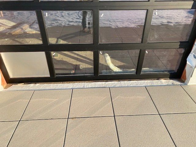 Black-framed glass door, partly open, with a tiled floor in front. A person's reflection is visible in the glass.