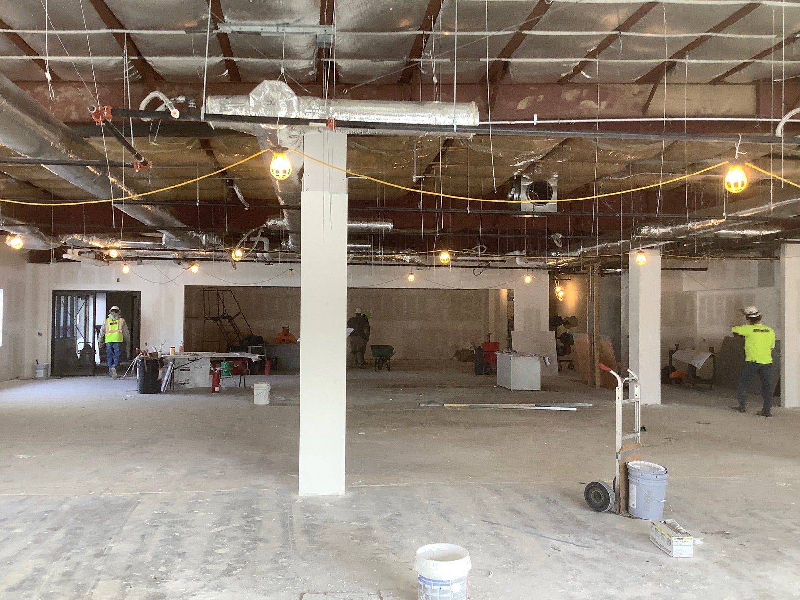 Interior construction site with workers, exposed ceiling, concrete floor, and central pillar.