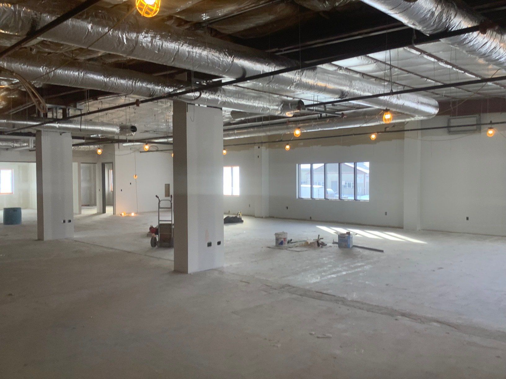 Interior of a building under construction. Concrete floor, white walls and pillars, exposed ceiling fixtures, and natural light from windows.