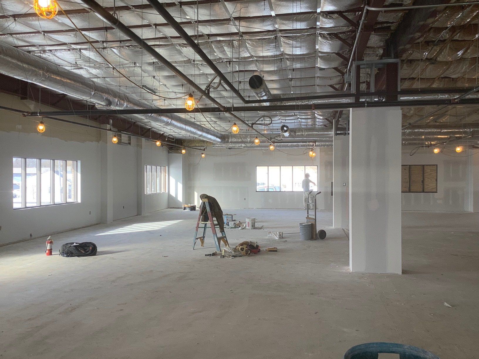 Interior construction site with workers, bare walls, exposed ceiling, and natural light.