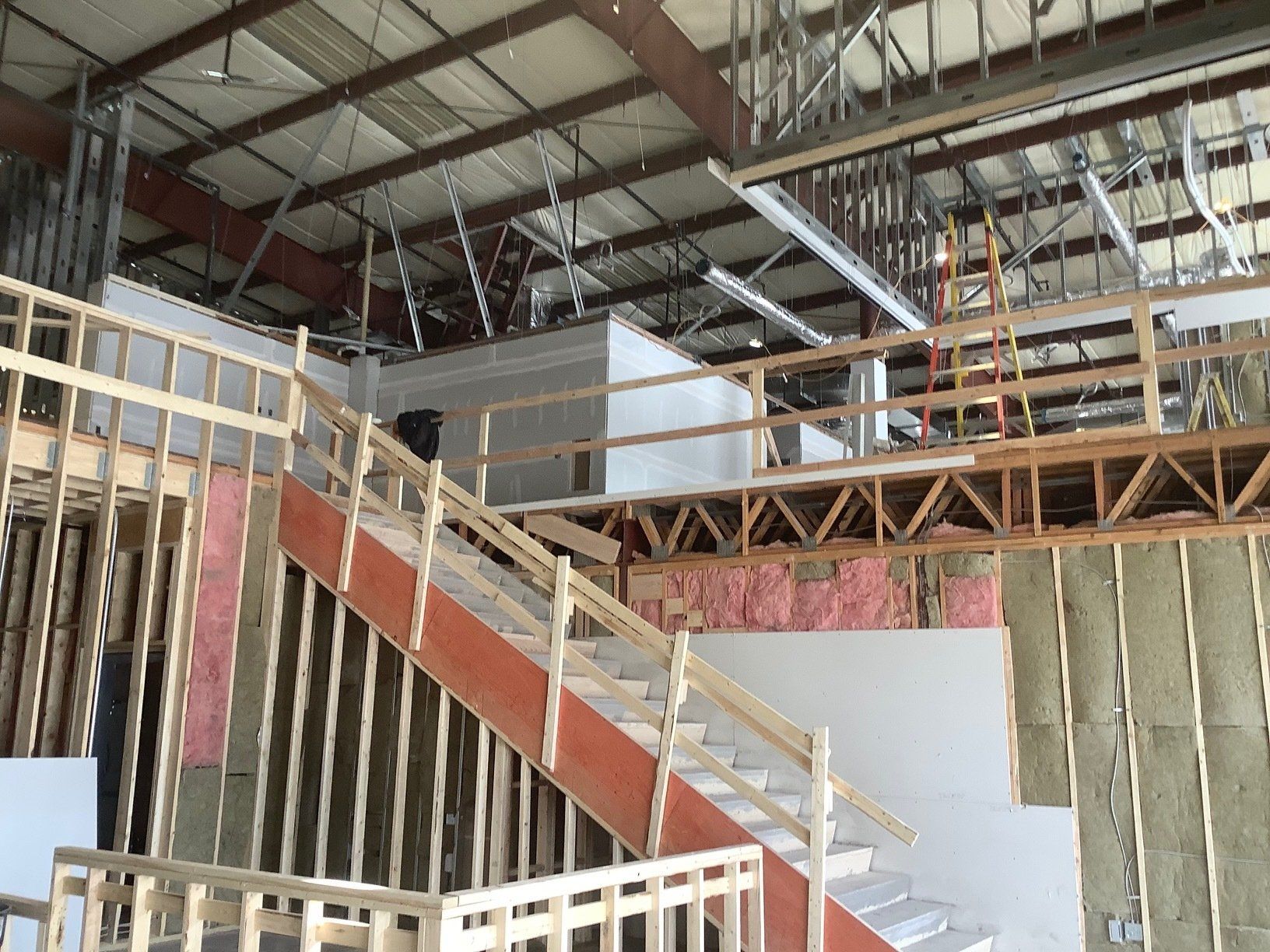 Interior of a building under construction, showing wooden framing, stairs, insulation, and exposed metal beams.