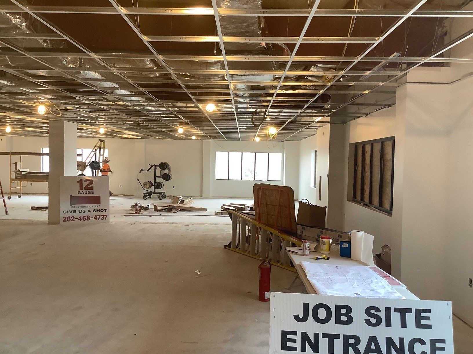 Interior of a construction site with exposed ceiling grid, drywall, and a job site entrance sign.