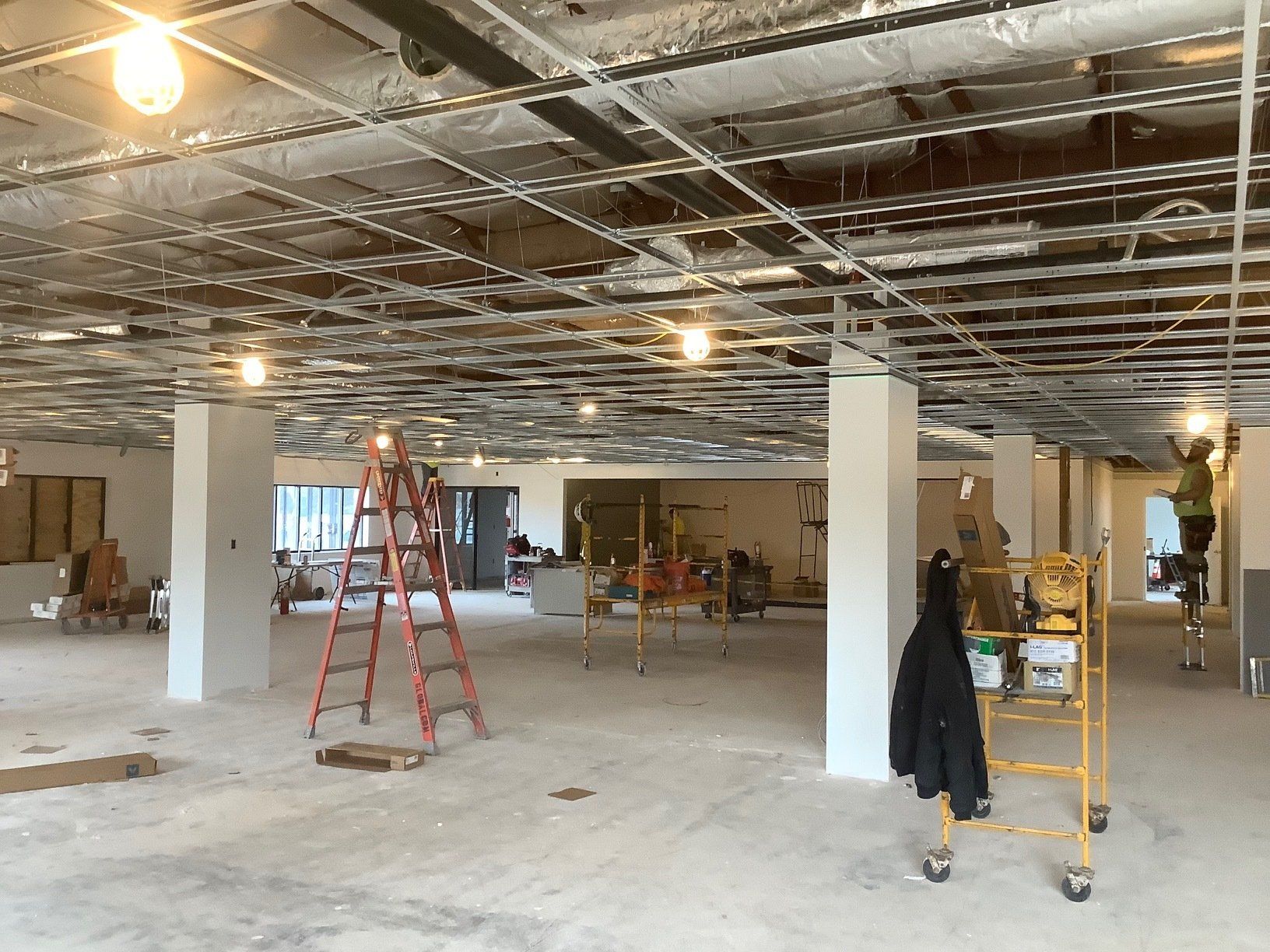 Construction site: unfinished interior with workers, ladders, and exposed ceiling framework.