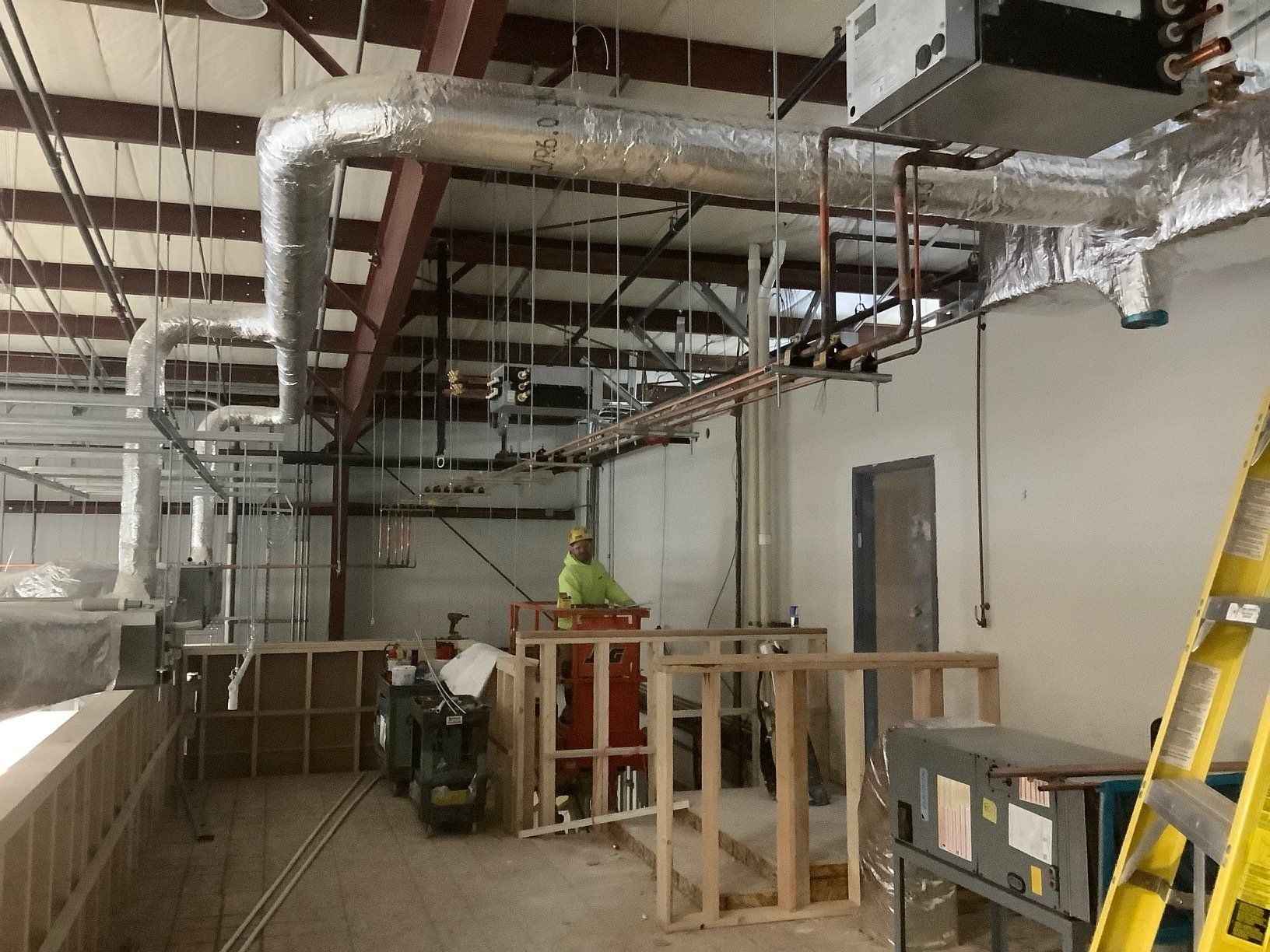 HVAC ductwork and piping in a commercial building under construction; a worker stands near equipment.