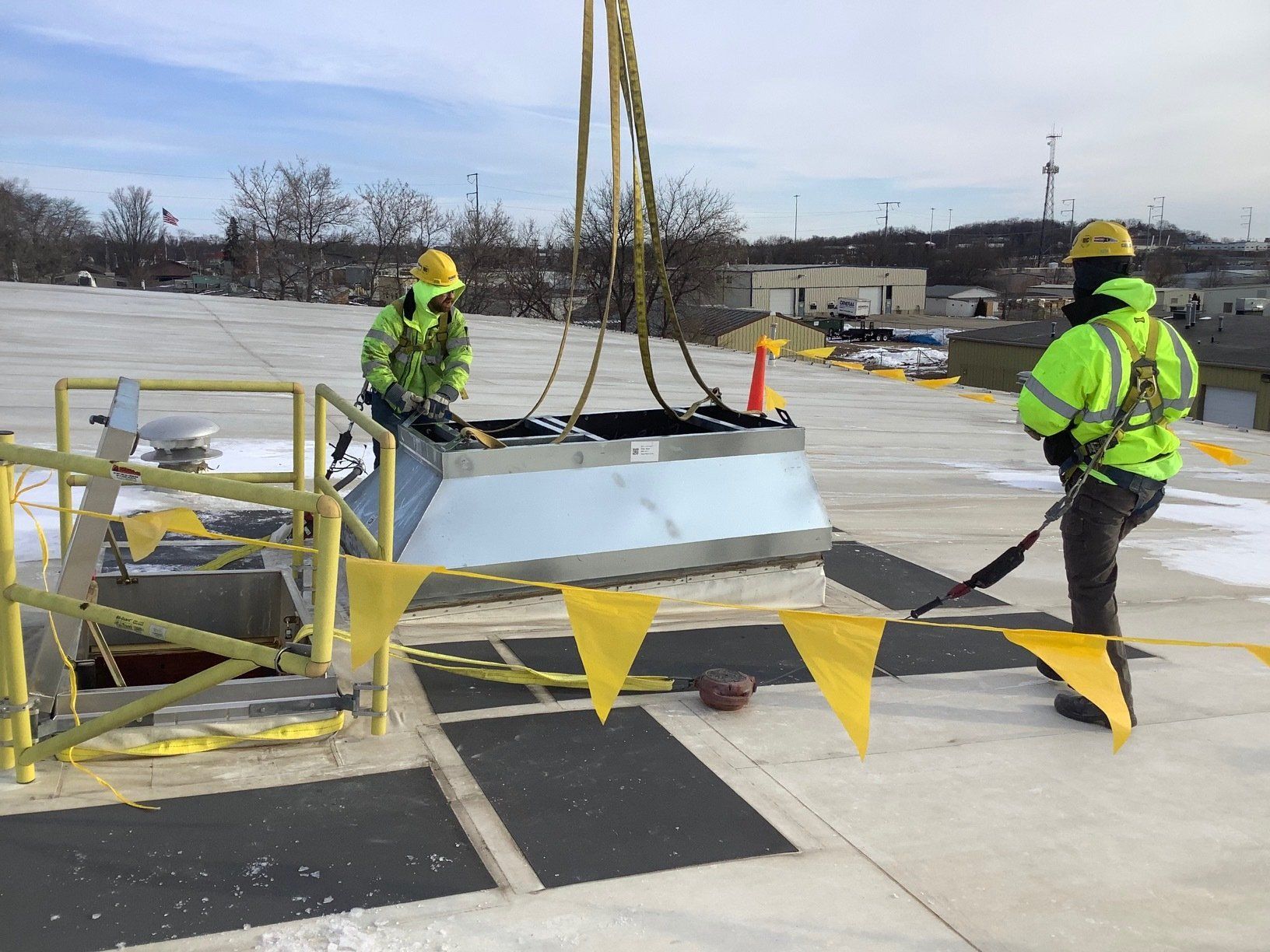 Workers on a rooftop using a crane to lift equipment. They are wearing safety gear.