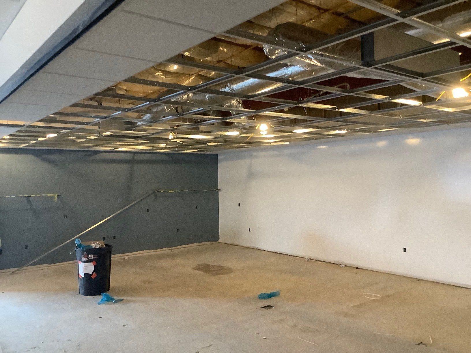 An unfinished room with a partially removed ceiling, grey and white walls, and a concrete floor.