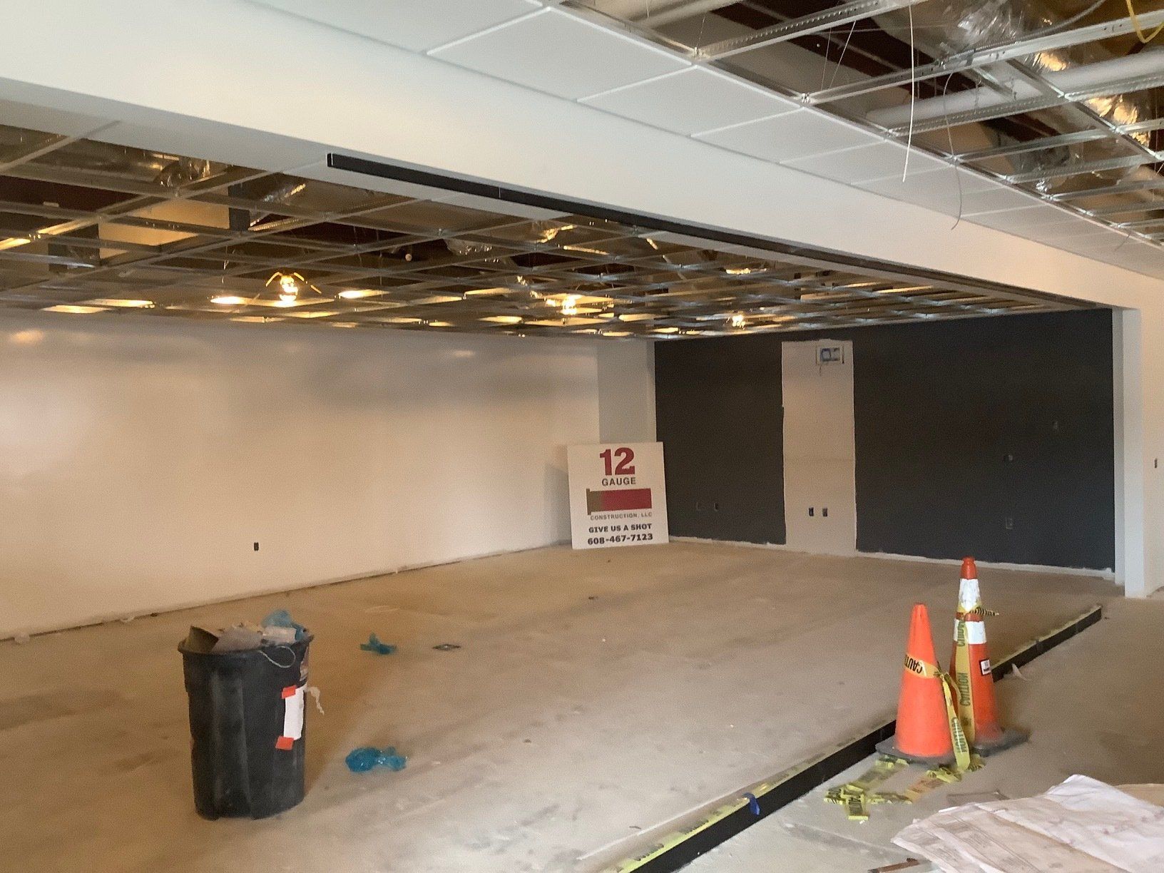 Unfinished interior with concrete floor, white and gray walls, exposed ceiling, construction debris, and cones.