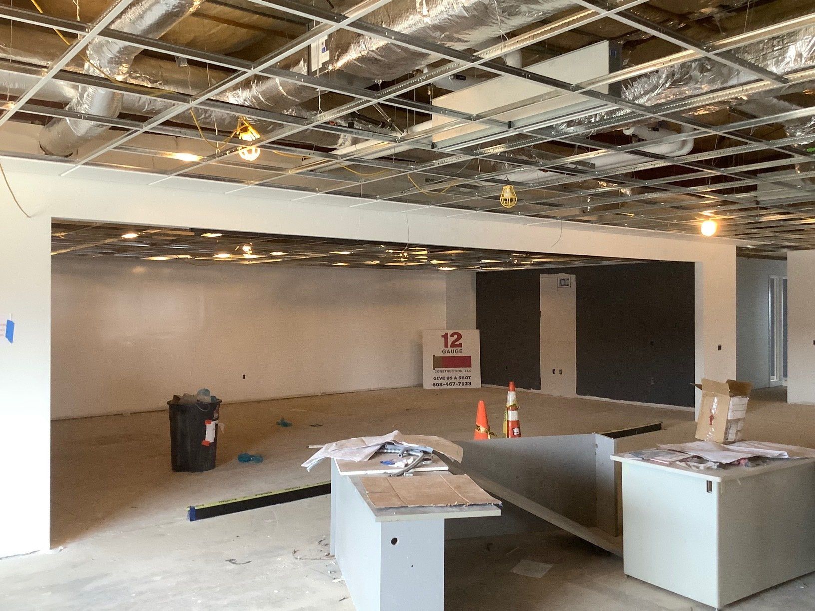Interior of a building under construction, showing unfinished ceiling, drywall, and debris on the floor.