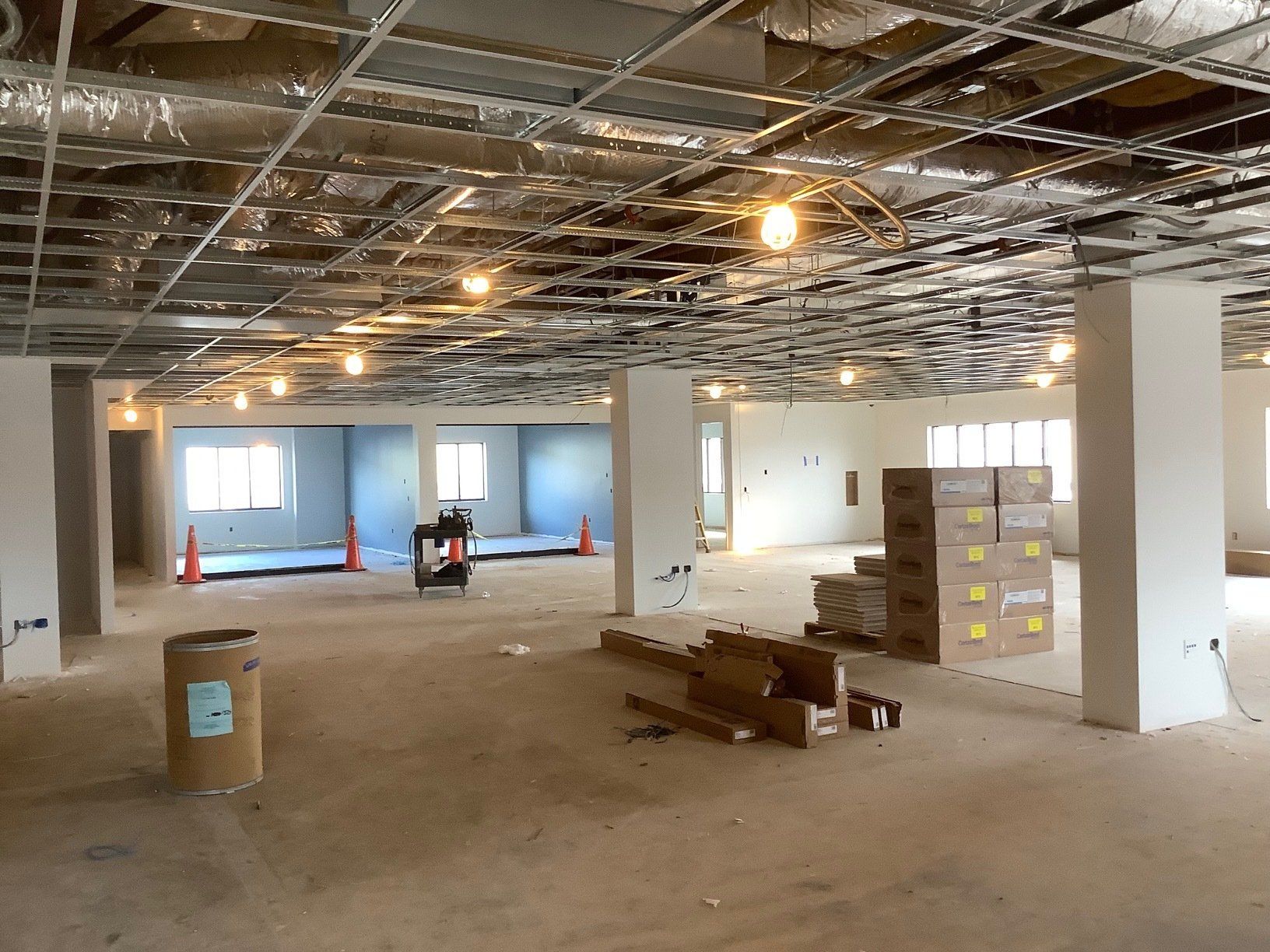 Interior construction site with exposed ceiling grid, pillars, and boxes.