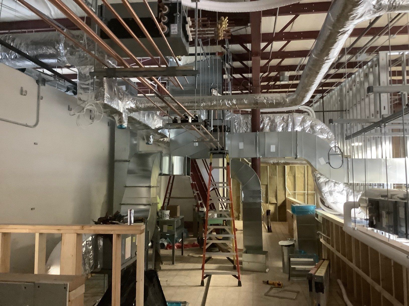 Interior construction site, exposed HVAC system and ductwork visible, ladder in the center.