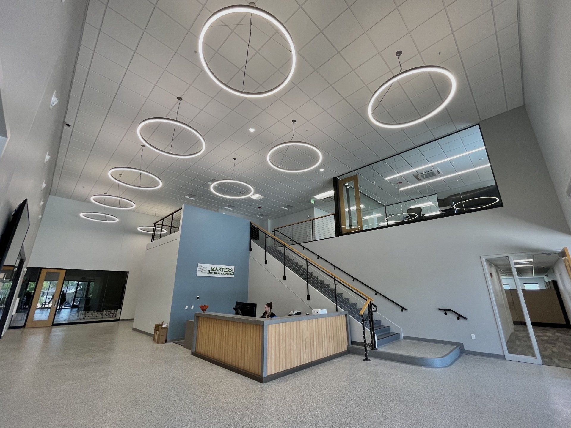 Lobby with reception desk, staircase, and circular lights in a modern building.