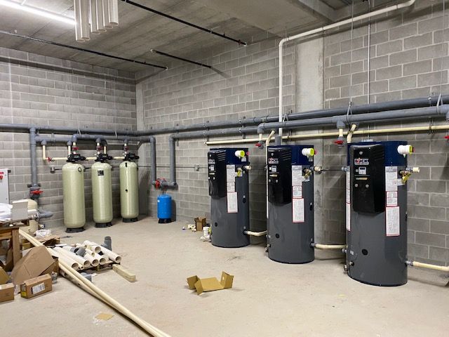 Water tanks and piping in a utility room with exposed brick walls.