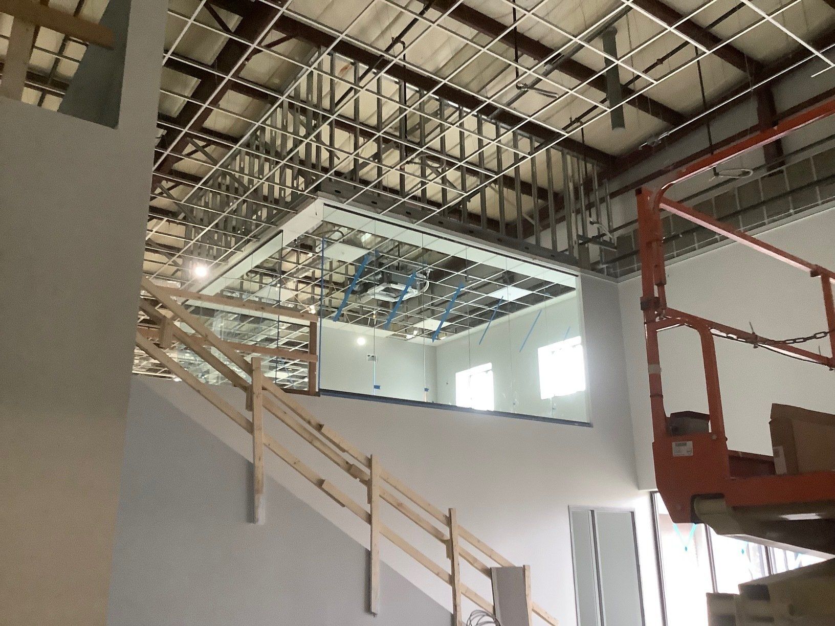 Interior view of a building under construction, showing a staircase, ceiling framework, and a lift.