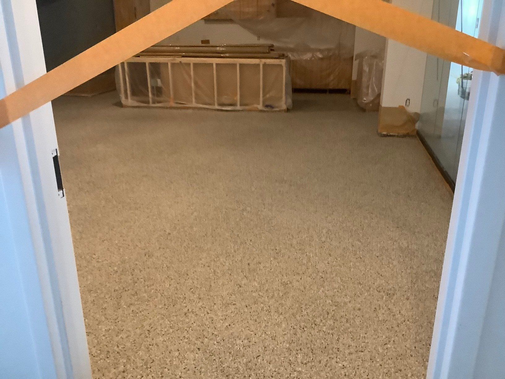 A room with a speckled floor, viewed through a doorway. Construction materials visible in the background.