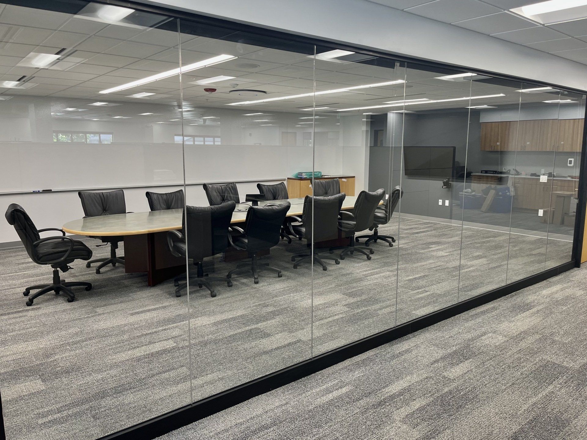 Conference room with glass walls, oval table, black chairs, and gray carpet.