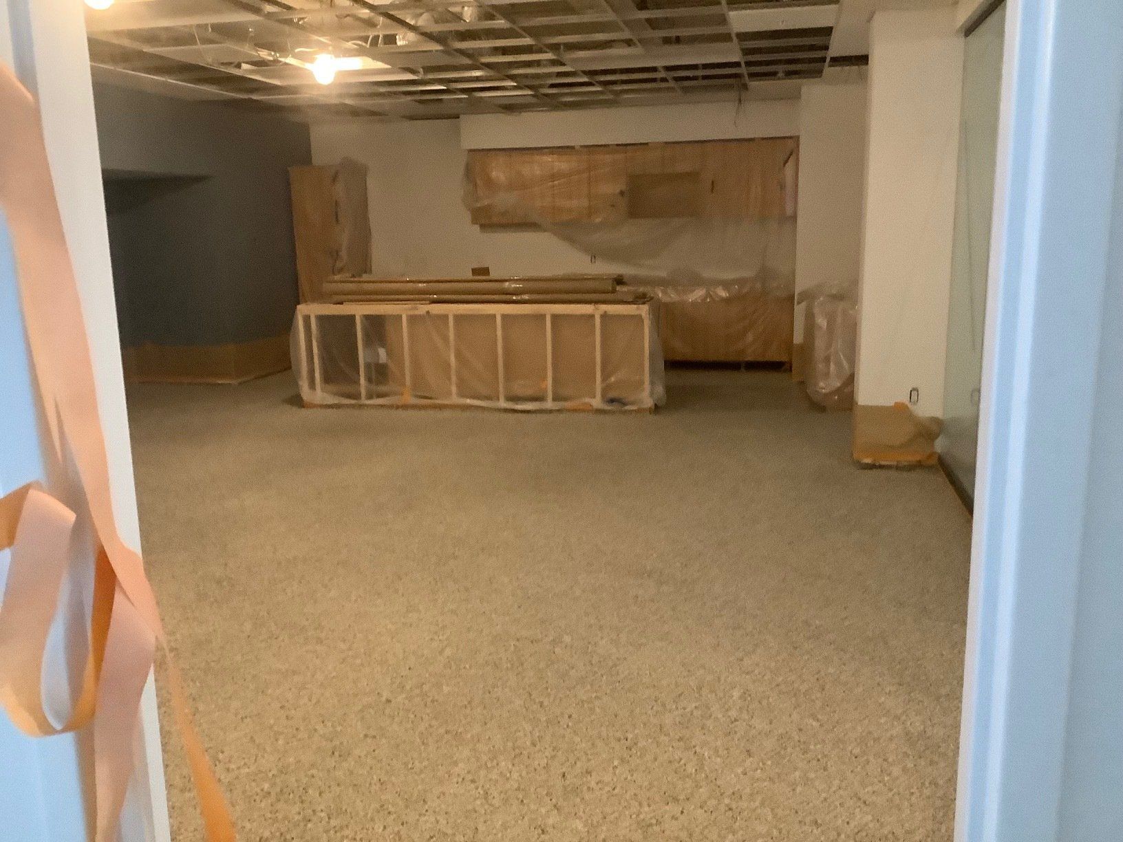 Empty room under construction with exposed ceiling, concrete floor, and wrapped elements.