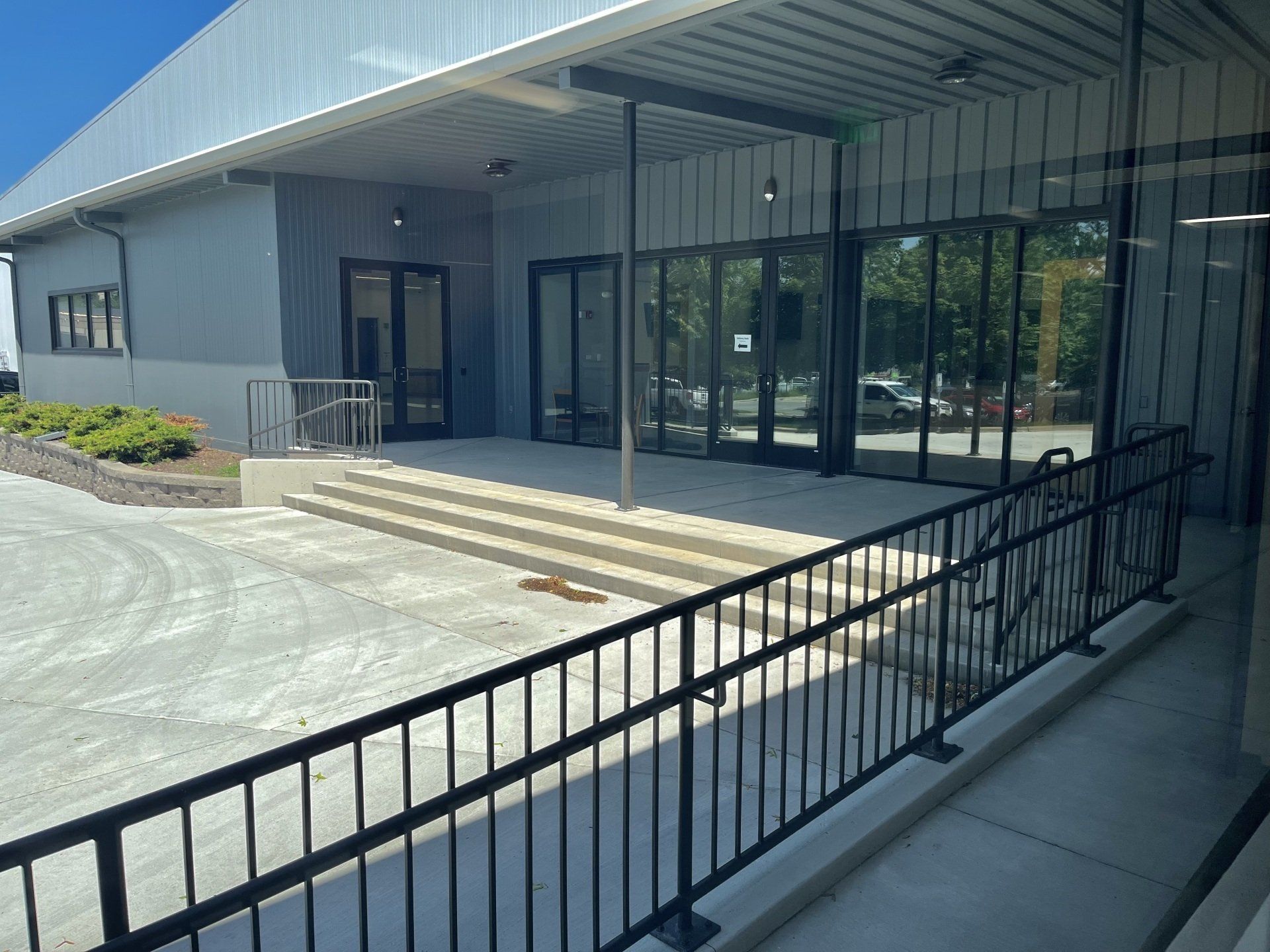 Exterior view of a building with a ramp, stairs, and glass doors. Gray and white colors.