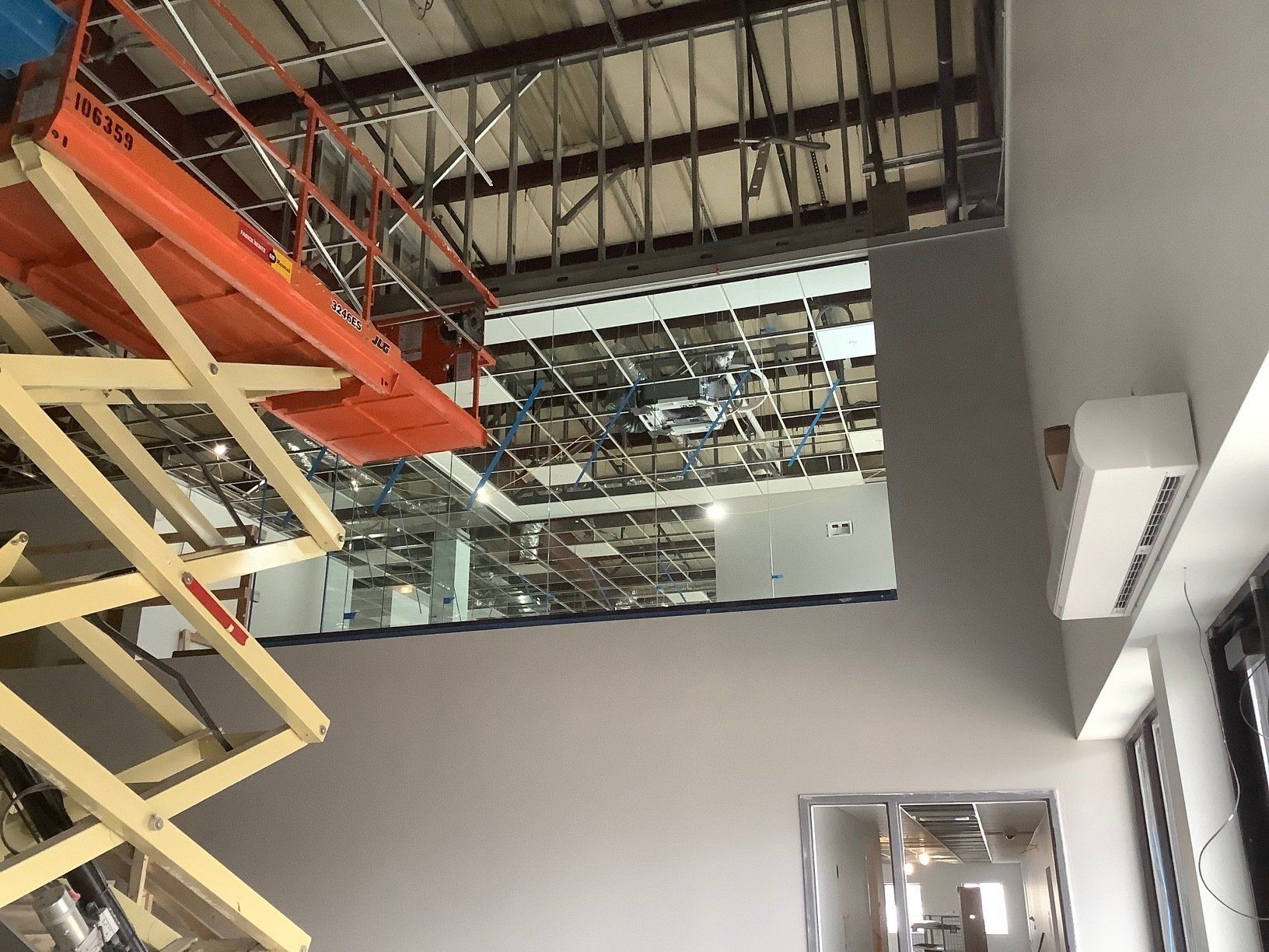 Orange lift platform near ceiling opening in a building under construction. White walls, exposed metal beams.