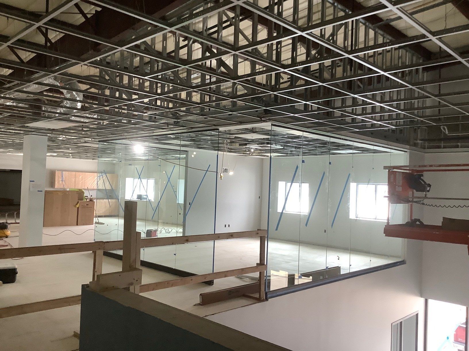 Construction site: metal ceiling framework, drywall walls, windows, unfinished floor, safety barrier.