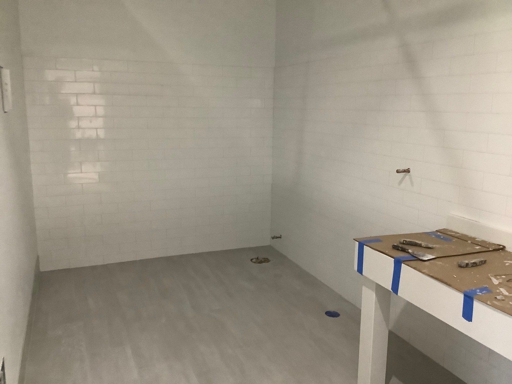 Empty room with white tiled walls, gray floor, and a white counter with tools.
