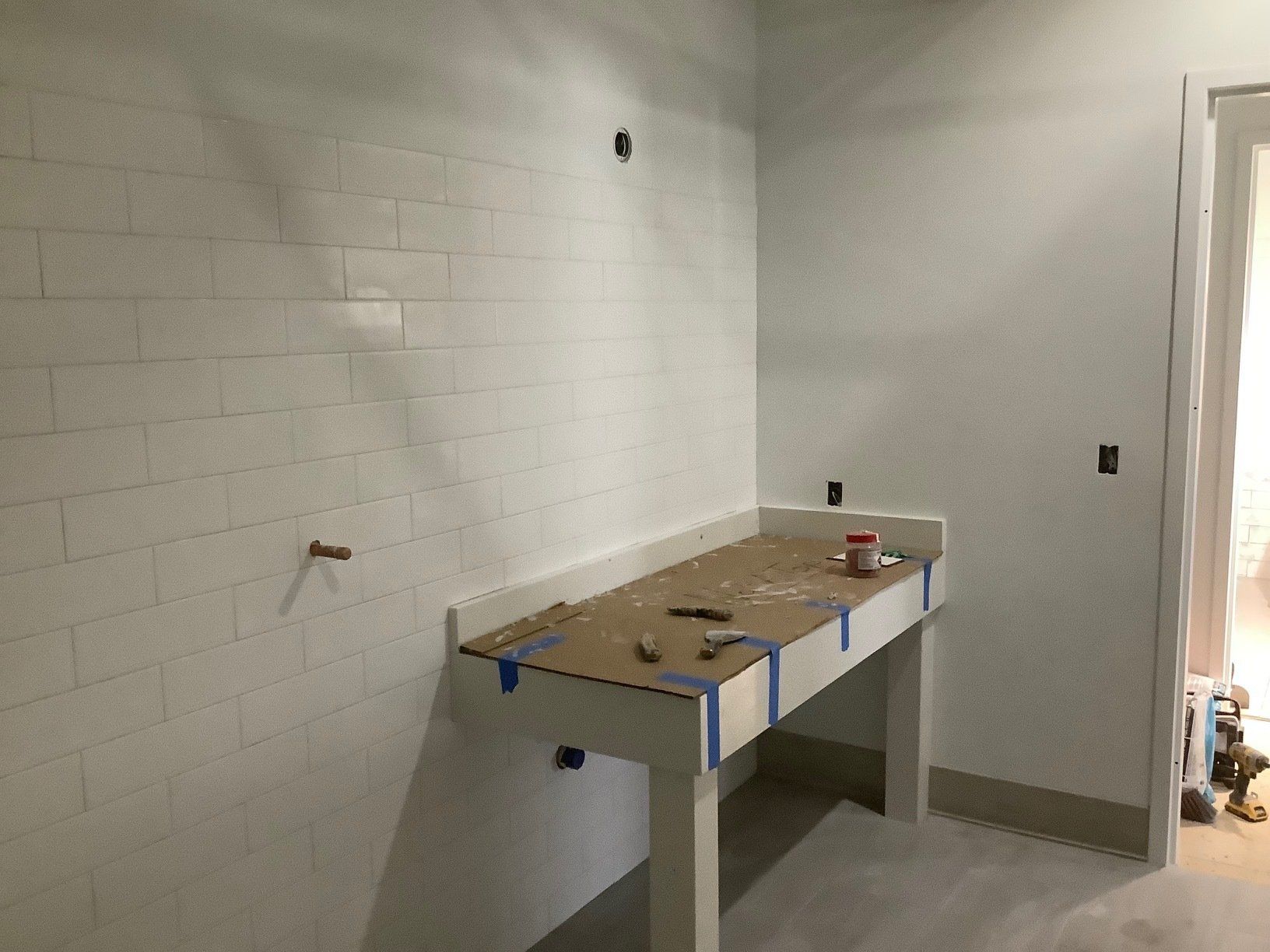 White tiled wall with a wooden table, construction in process.