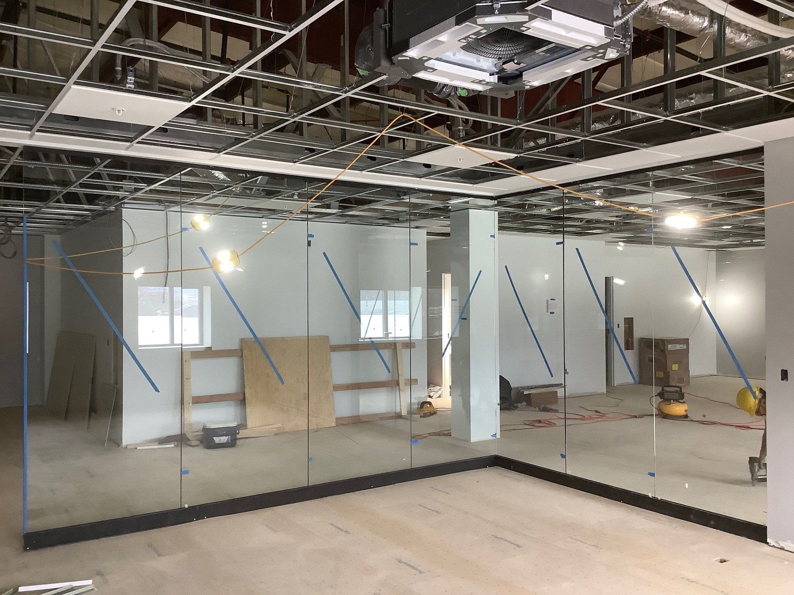 Interior construction of a room with floor-to-ceiling glass panels and exposed ceiling.