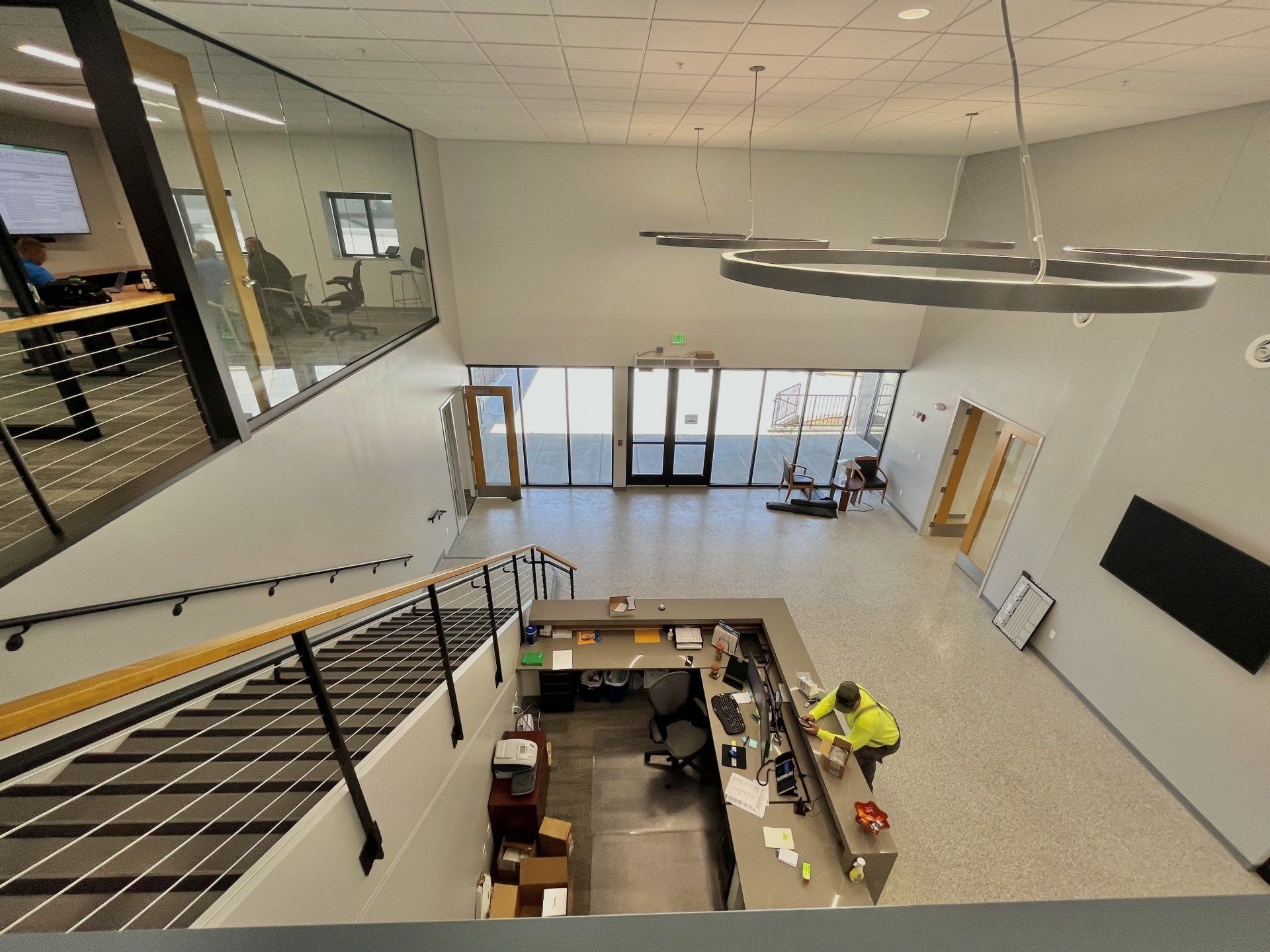 Lobby with reception desk, staircase, and exterior doors. A person in a yellow vest works at the desk.