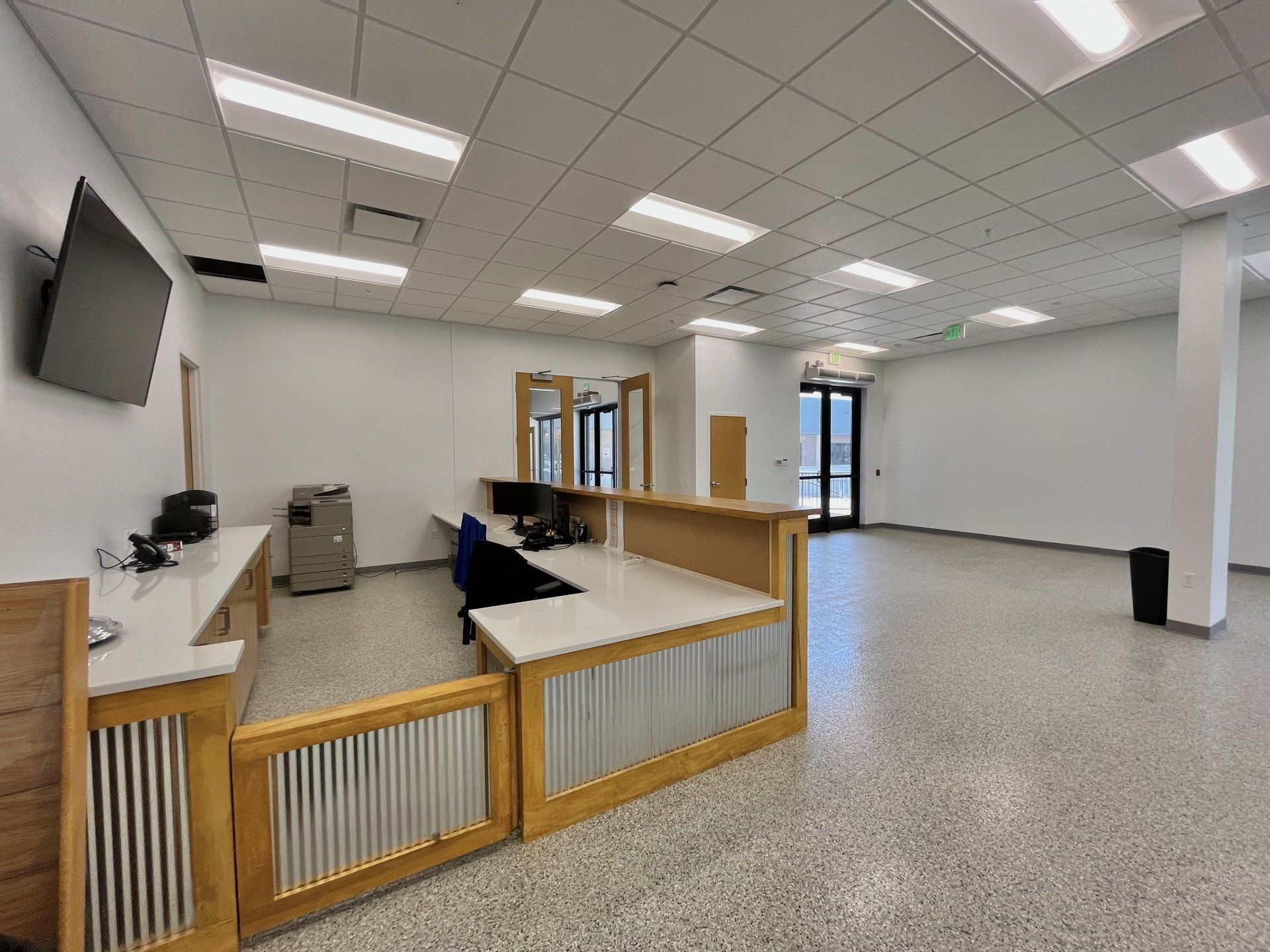 A modern office reception area with a reception desk, gray flooring, and white walls.