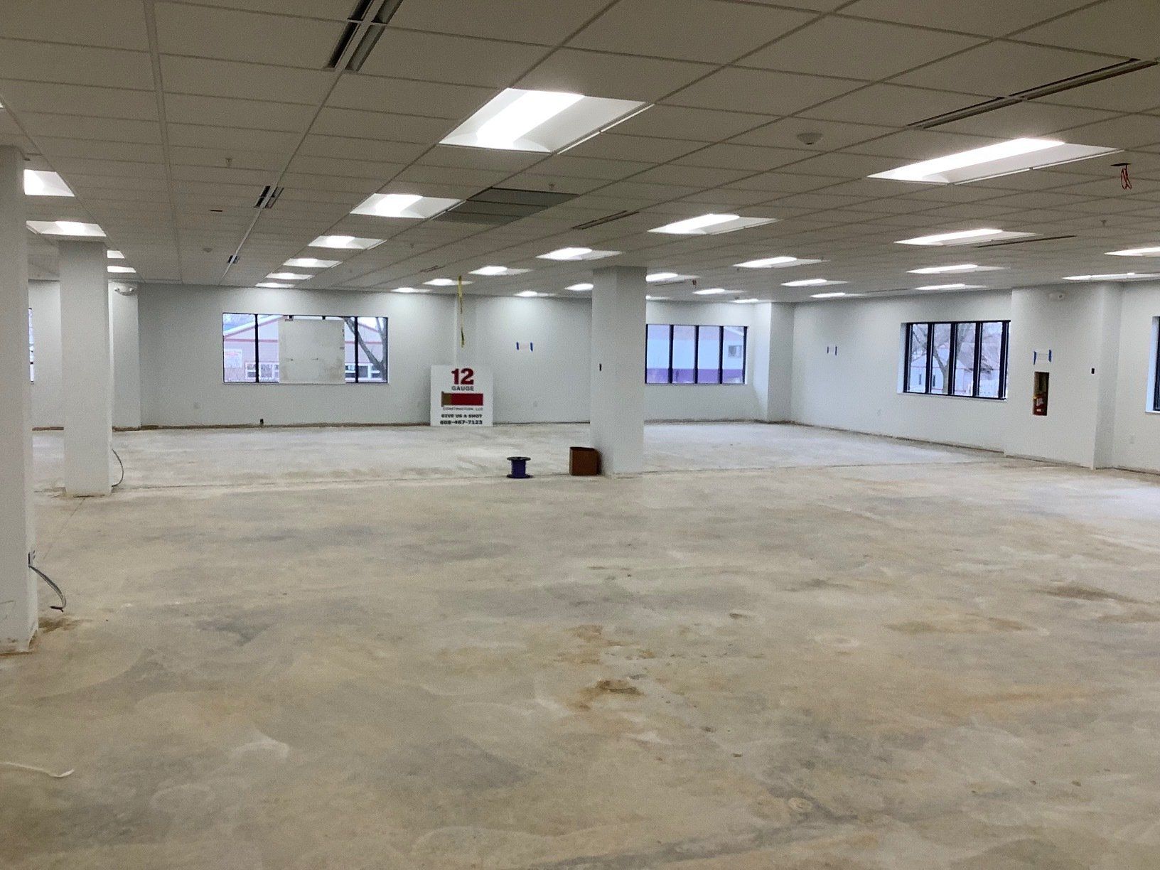 Empty, open office space with concrete floor, white pillars and walls, overhead lights.