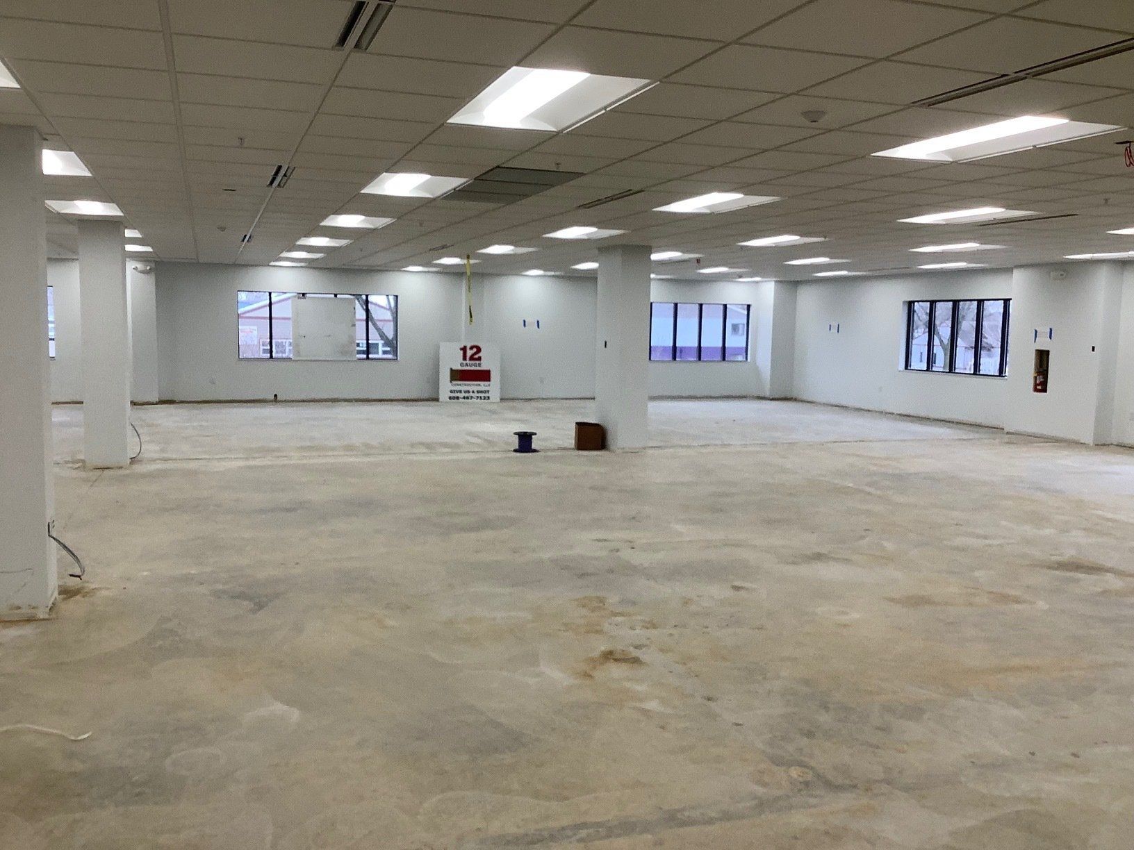 Empty, open interior space with concrete floor, white walls, support pillars, and ceiling lights.