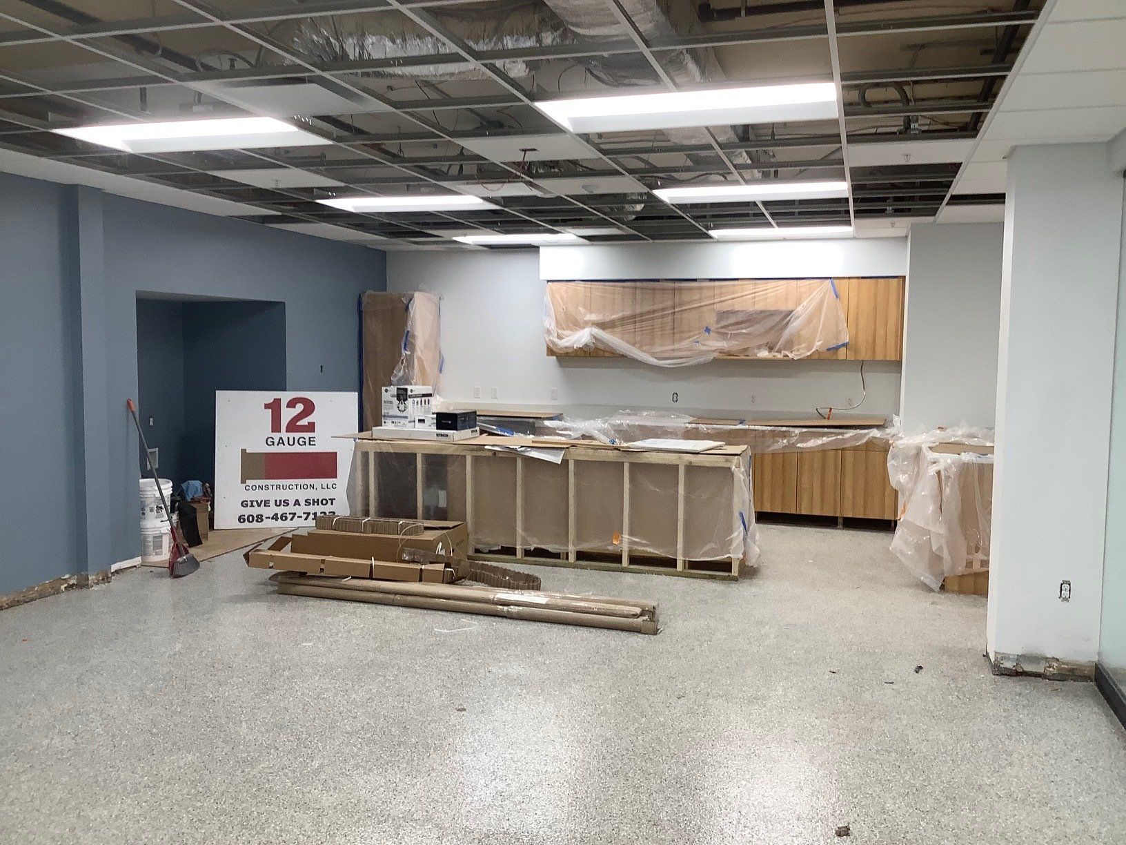 Interior of a room under construction with cabinets, exposed ceiling, and a sign. Blue and tan colors.