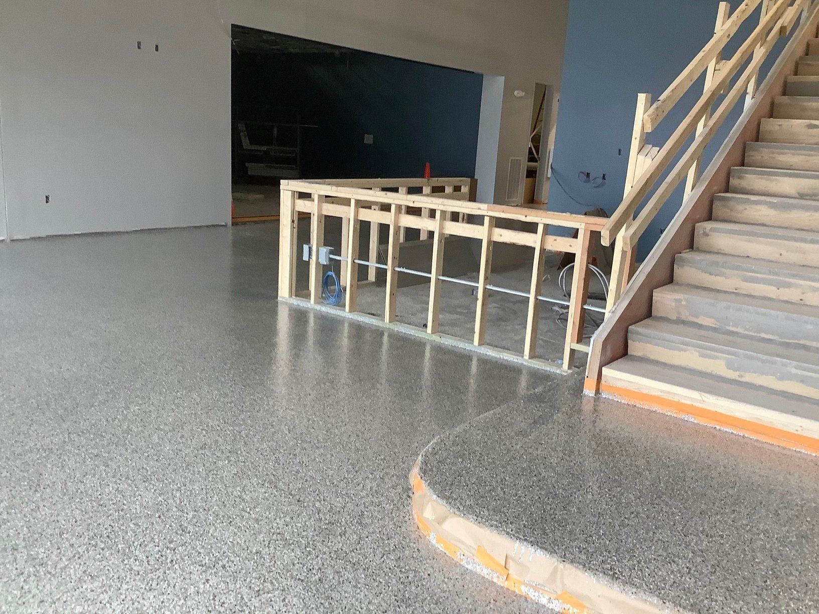 Polished concrete floor in a building under construction, with a wooden staircase and partial railing.
