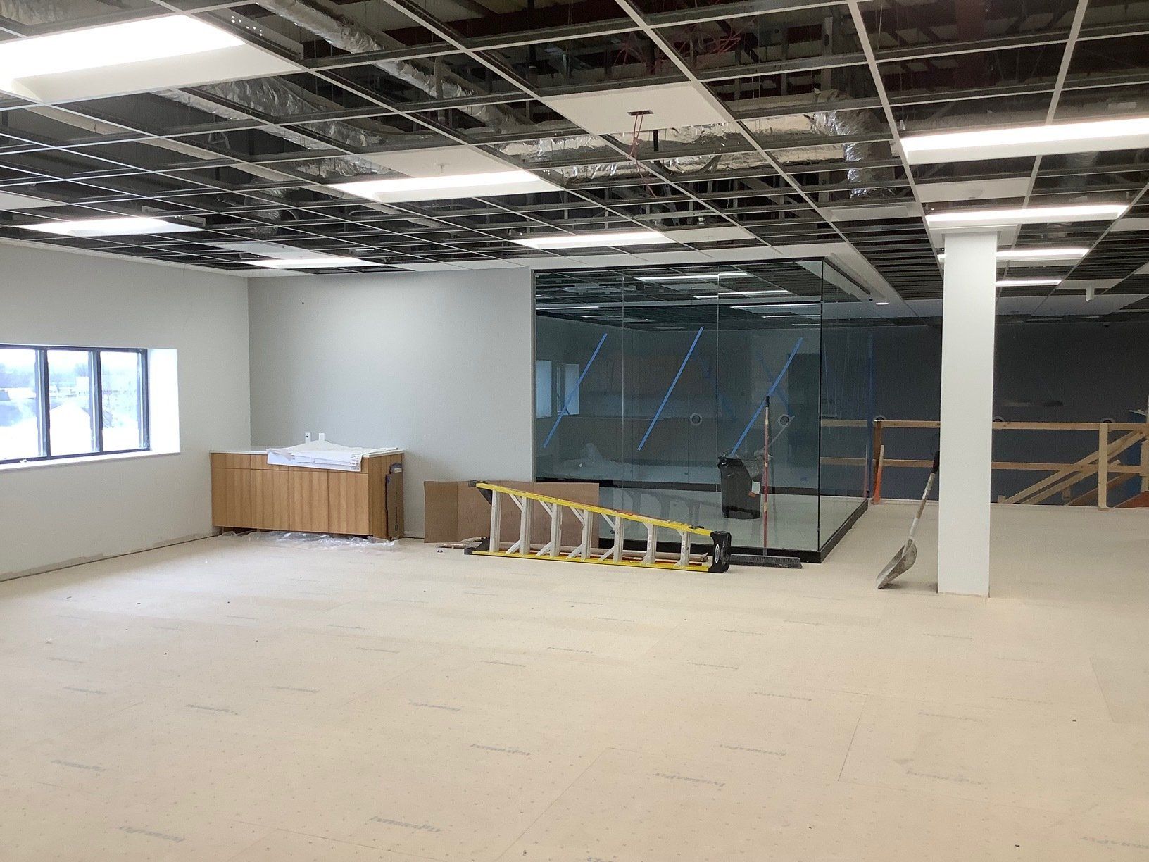 Interior view of a construction site with exposed ceiling, cabinets, and a partially built glass room.