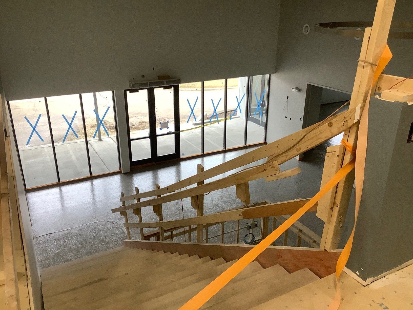 Interior view of a building under construction. Staircase with wooden handrails leads to a glass door.
