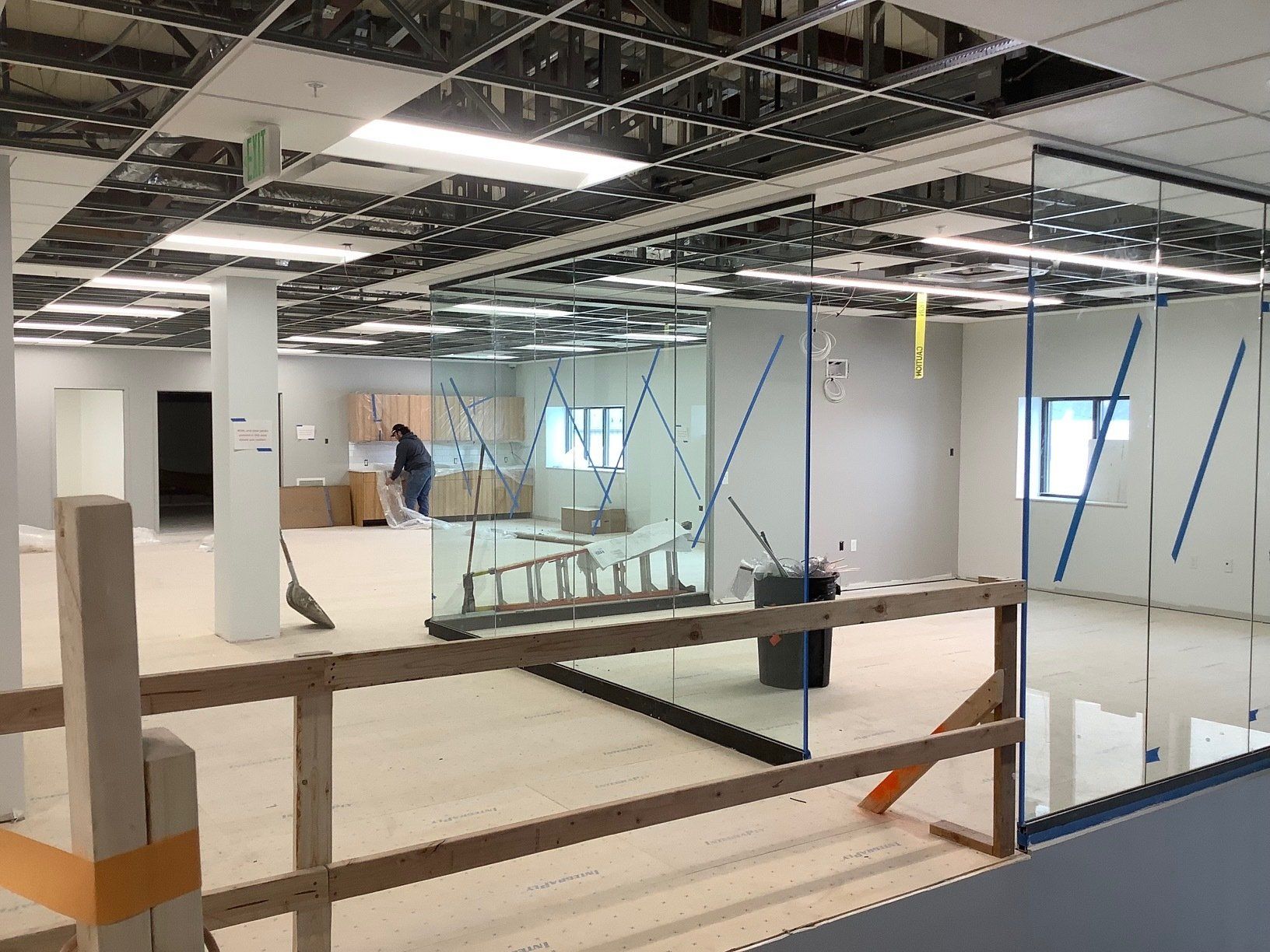Office construction: worker sweeping, glass walls, exposed ceiling, unfinished floors, safety rail.