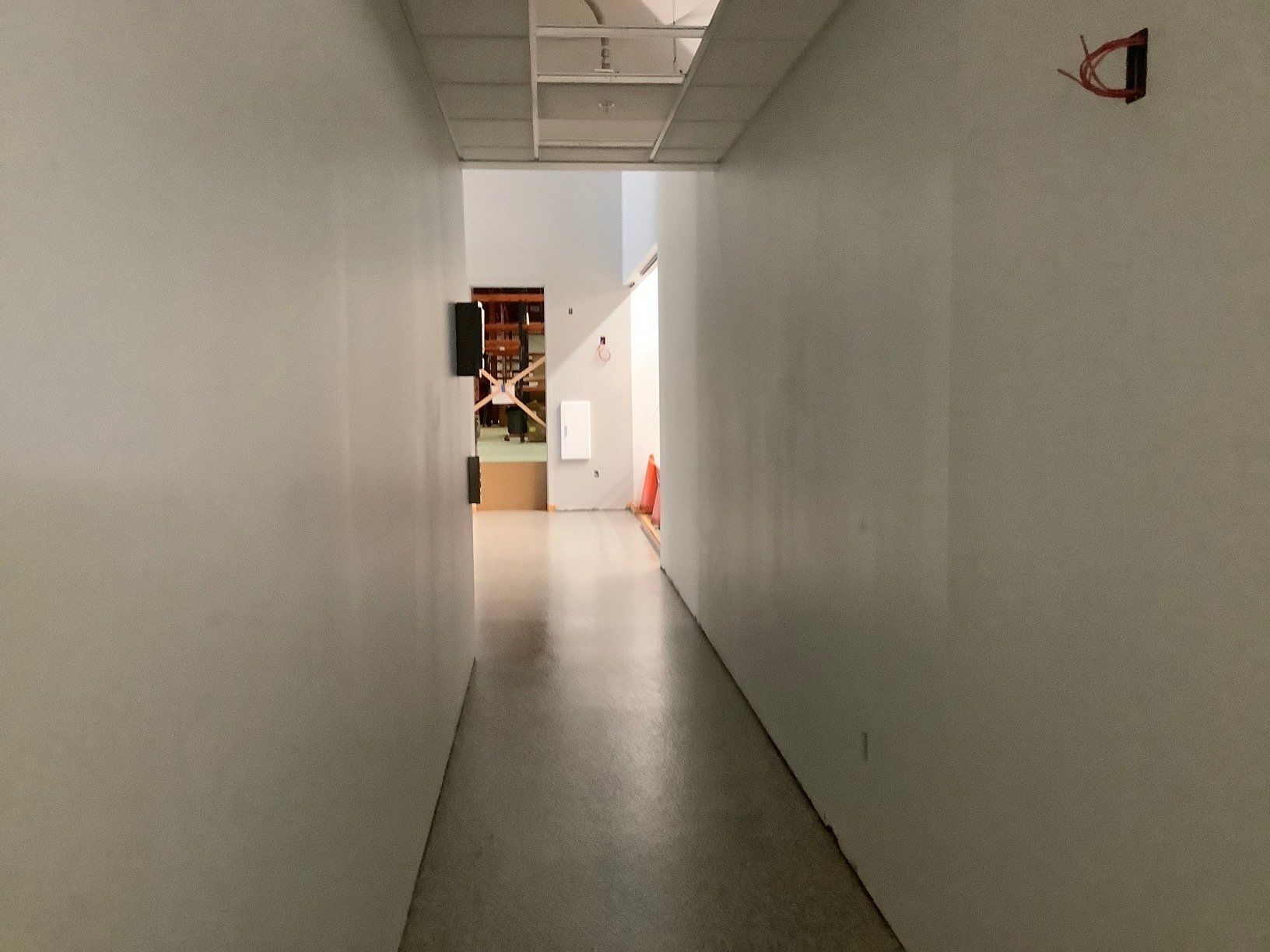 Narrow hallway with white walls and a shiny floor. Light at the end.