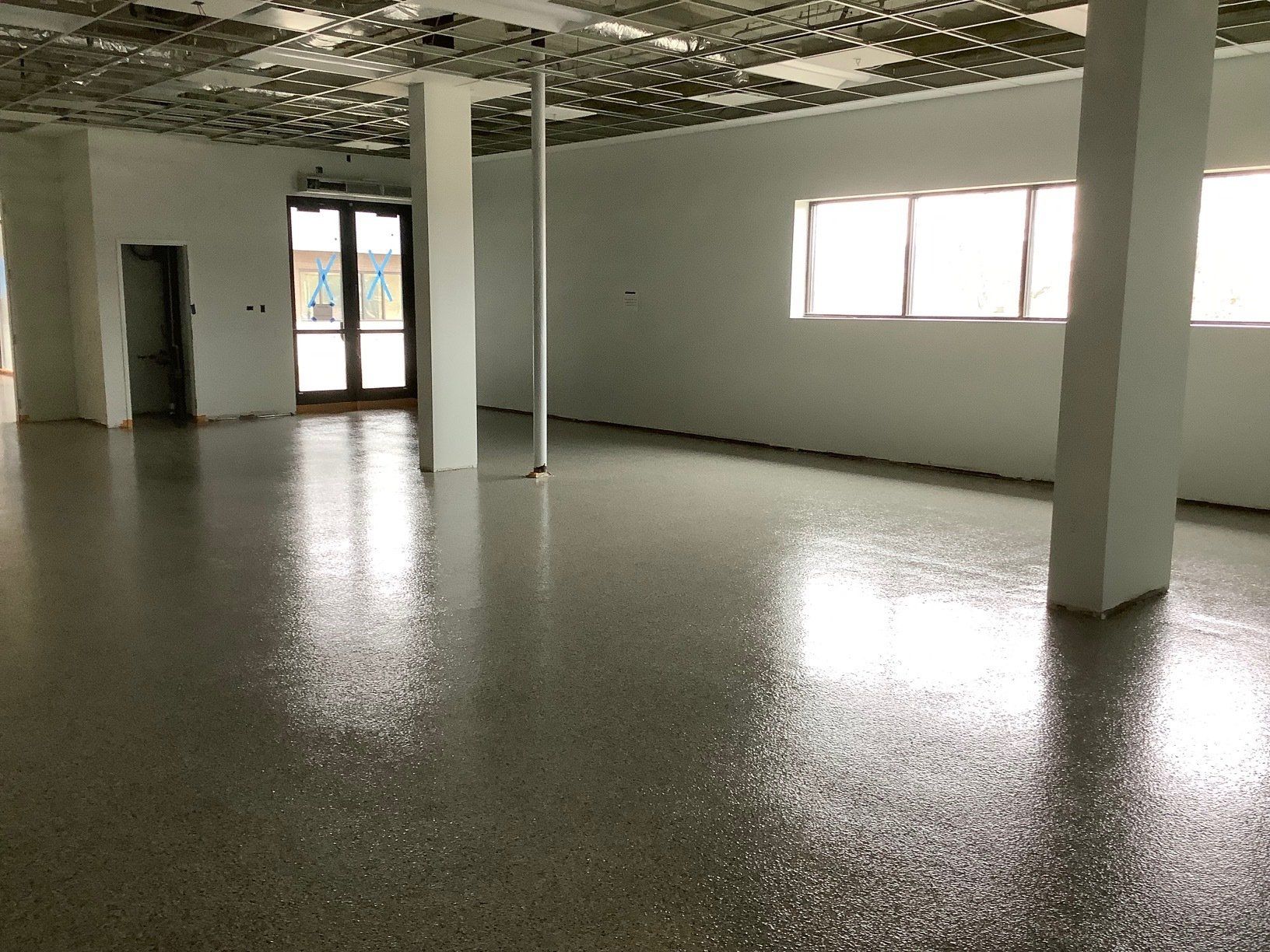 Open room with polished concrete floor, two pillars, windows, and damaged ceiling tiles.