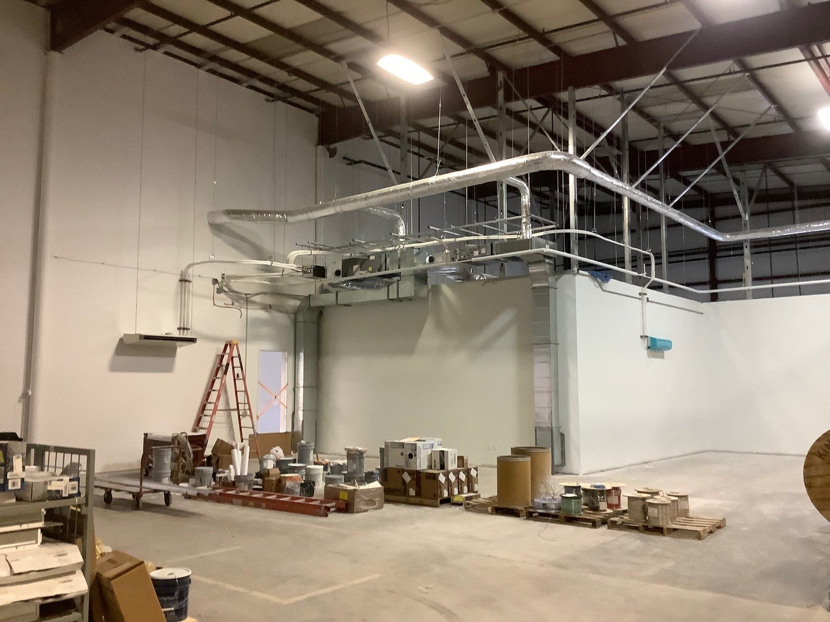 Interior view of an unfinished industrial building with pipes, equipment, and construction materials.