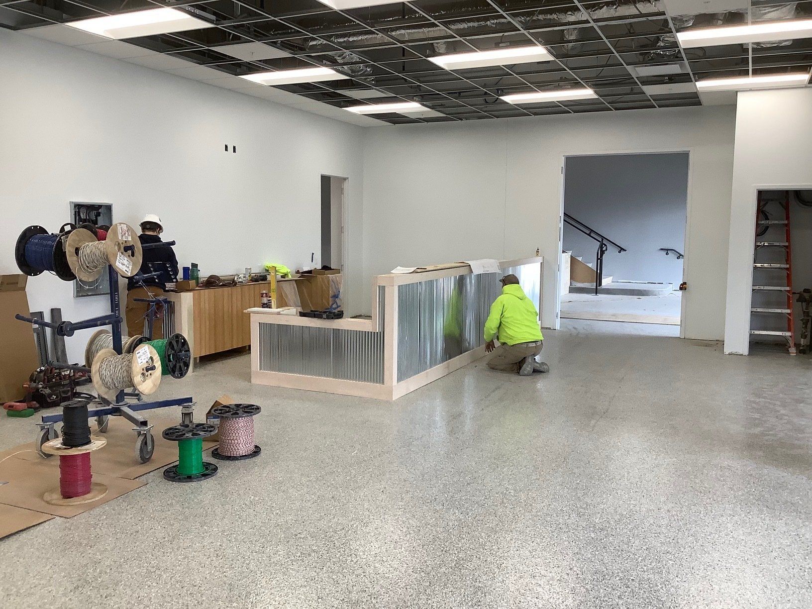 Construction site interior with workers; exposed ceiling, wire spools, and unfinished counter.