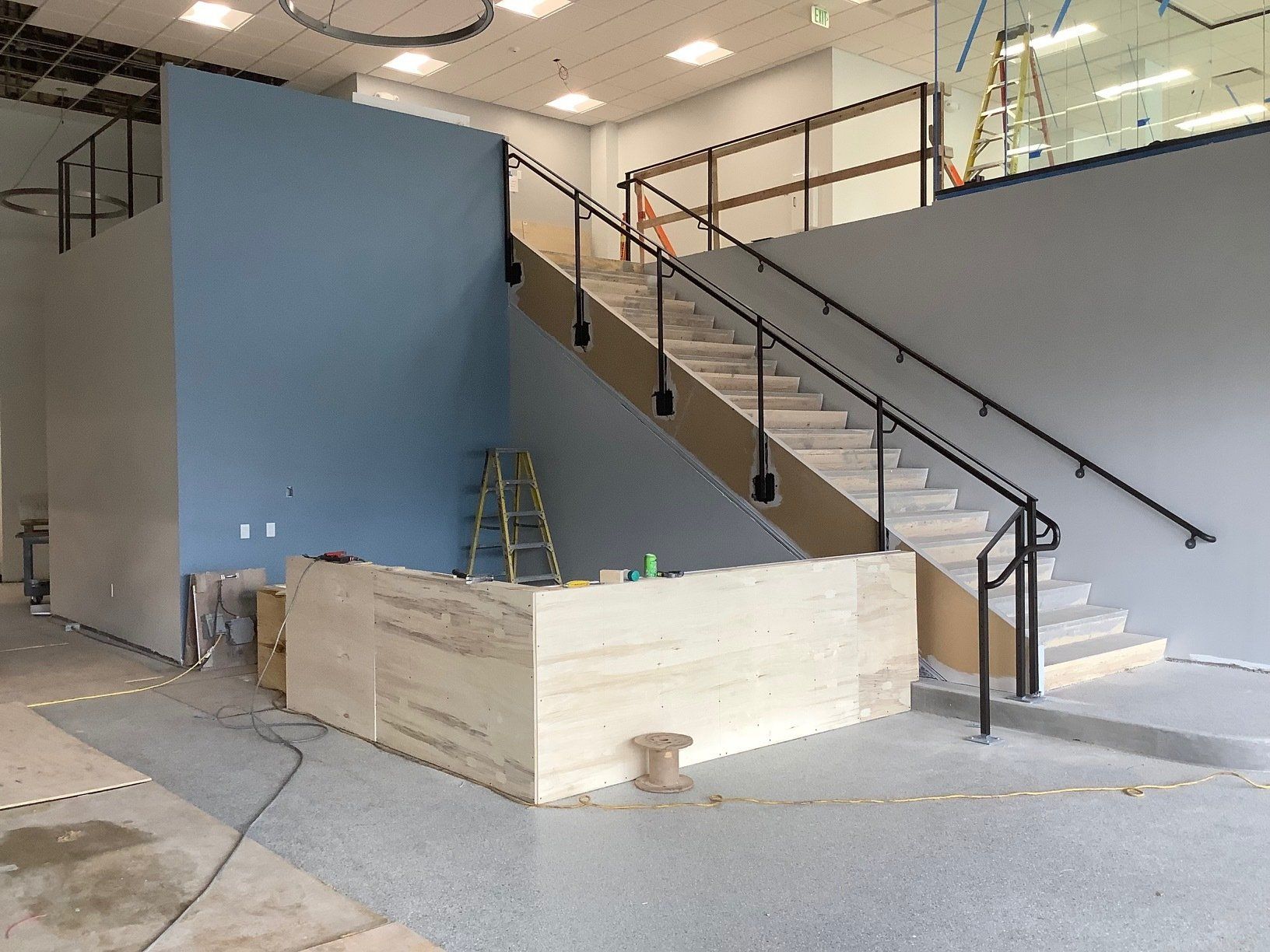 Interior with stairs, blue wall, tan and gray tones, handrails. Construction in progress.