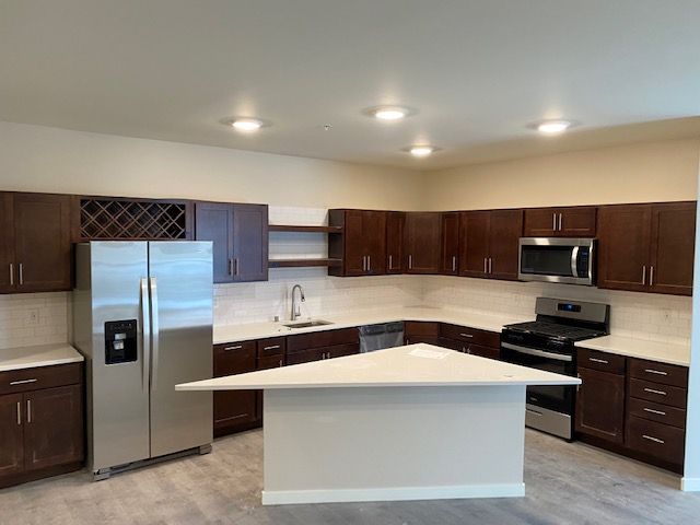 Modern kitchen with dark brown cabinets, stainless steel appliances, white countertops, and an island.