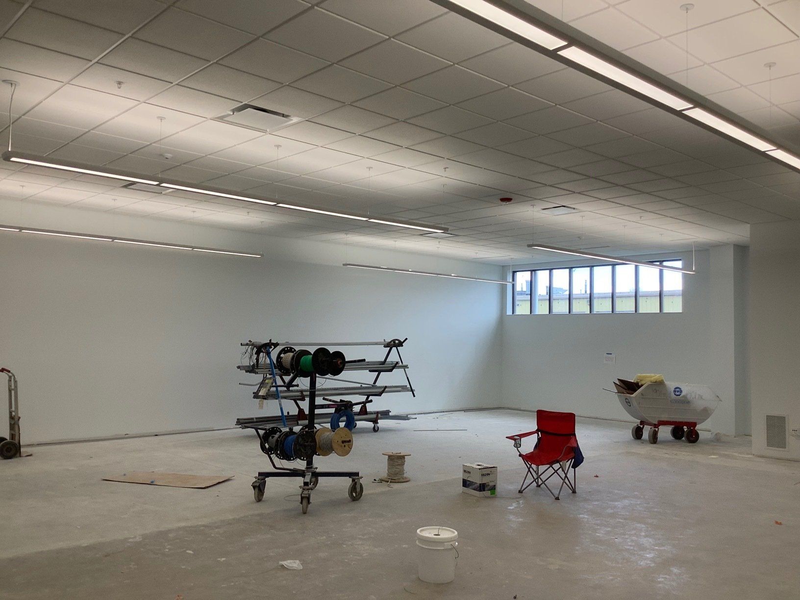 Empty room with white walls, exposed ceiling lights, and construction equipment.