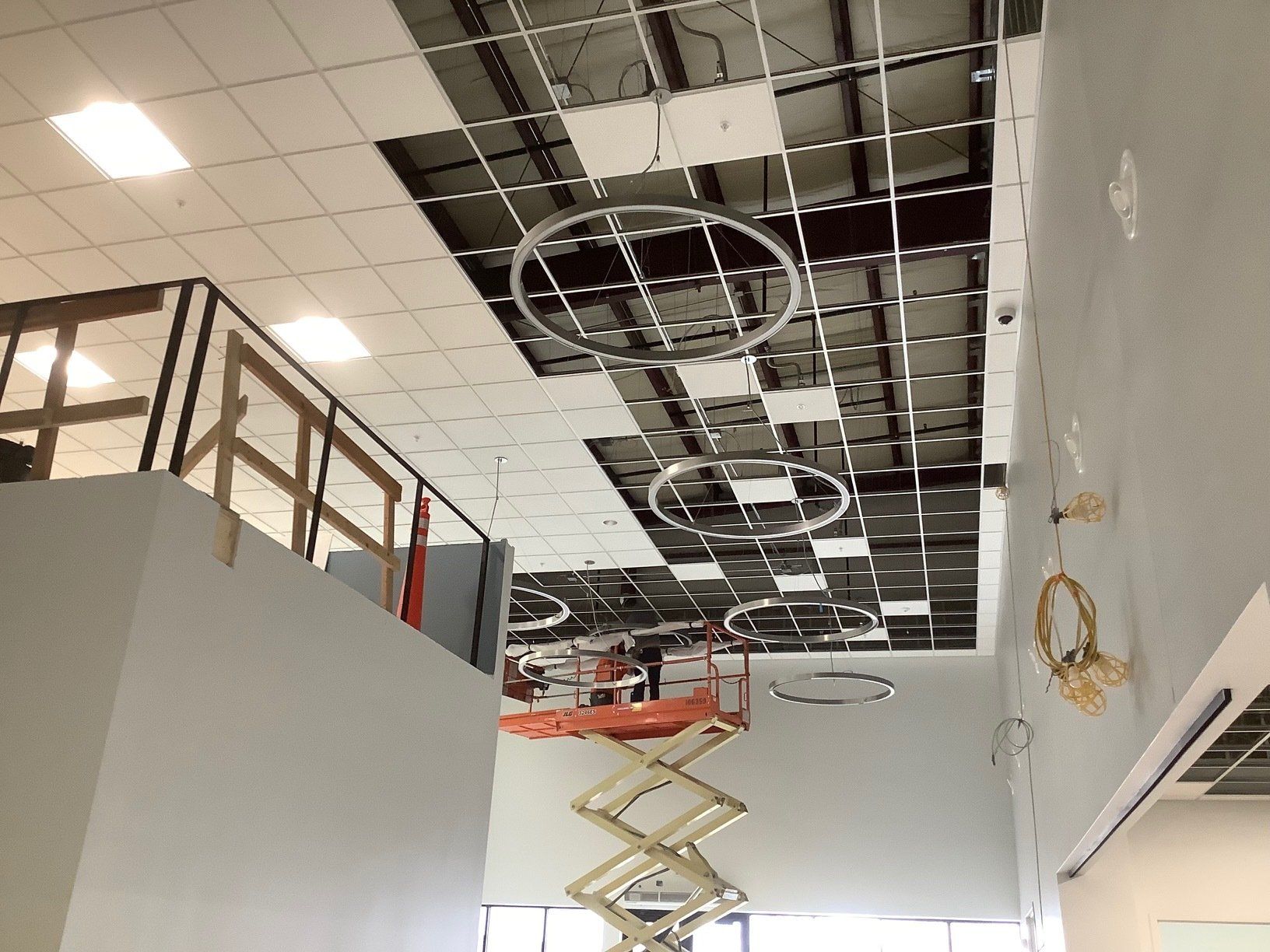 Construction site: ceiling grid with missing tiles; lift; decorative circular lights; interior.