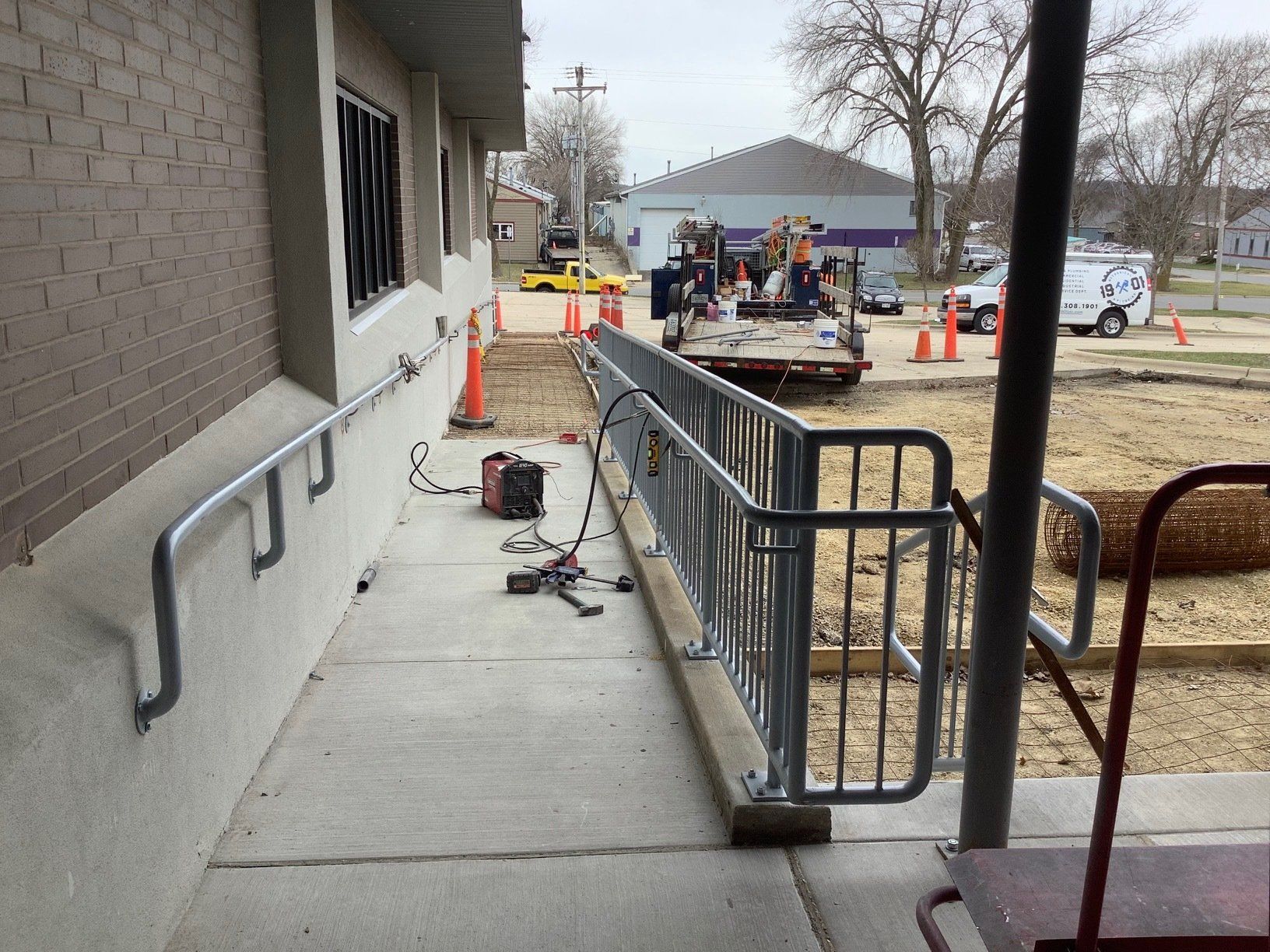 Exterior view of a building with a newly constructed wheelchair ramp. Construction equipment and workers visible in the background.