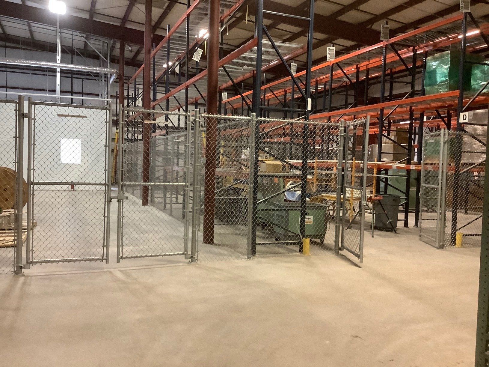 Warehouse interior with chain-link fence enclosures; shelving in background; concrete floor.