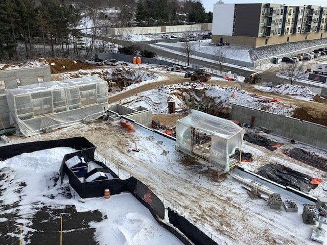 Construction site covered in snow, with buildings, earthmoving equipment, and protective enclosures.