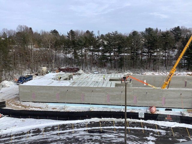 Construction site in winter with concrete foundation and crane. Snow covers the ground and surrounding trees.