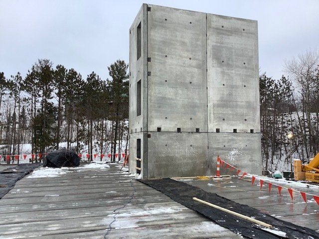 Concrete building structure outdoors, with window cutouts, on concrete and snow. Trees in background.