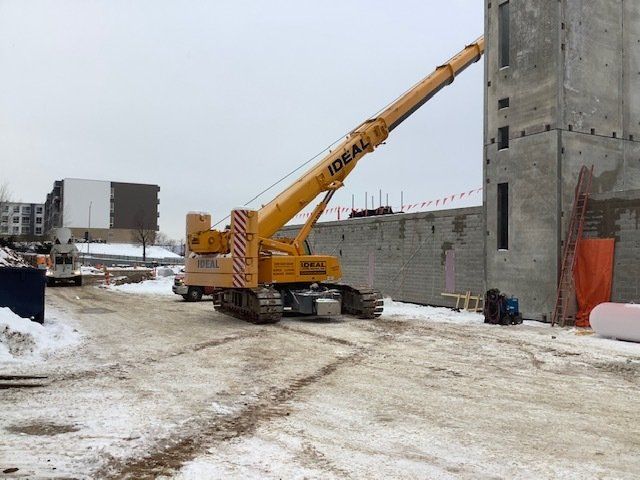Yellow crane lifting a large panel at a construction site on a snowy day.